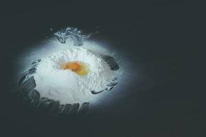 Egg yolk on flour. White flour pile and egg. Baking ingredients on wooden table. Broken egg on flour. photo