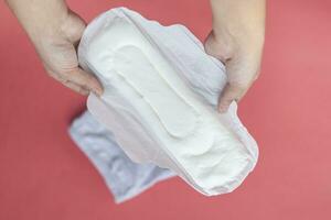 A white sanitary pad in woman's hands on a pink background with copy space. Absorbent item for women special days. Hygiene and health concept. photo