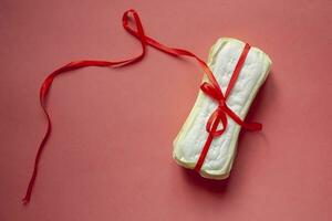 A stack of sanitary pads or Feminine hygiene pads tied with a red ribbon on a pink background. Critical days, Intimate, Period days concept photo