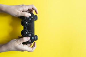 Hand holding video game controller on yellow background. Free space photo