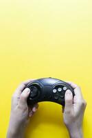 Vertical view to hands holding black gamepad and playing video game against yellow photo