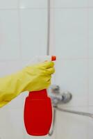 mujer con rociar limpiador. ama de casa participación rojo rociar botella a baño. limpieza bañera foto