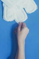 Young women taking sanitary pads inside of her cosmetic bag on blue background photo