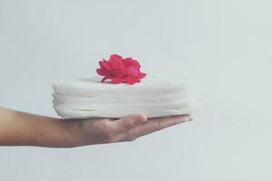 Woman's hand holding a stack of sanitary napkins with red rose on. Against white background. Period days concept showing feminine menstrual cycle. photo