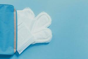 Female's hygiene products. Women's bag and sanitary pads on blue background photo