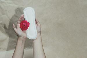 Female's hand holding sanitary napkins with red rose on it. Period days concept showing feminine menstrual cycle photo