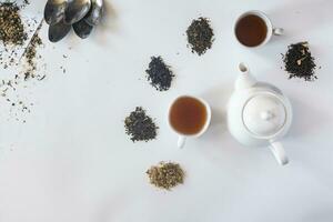 Tea set with white ceramic tea pot and other tea ingredients on the white. Flat lay view of various dried teas and teapot. View from above. Space for your text photo