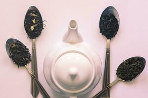 White ceramic tea pot and various dried teas on the white background. Flat lay view. Space for your text photo