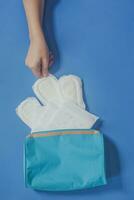 Young women taking sanitary pads inside of her cosmetic bag on blue background photo