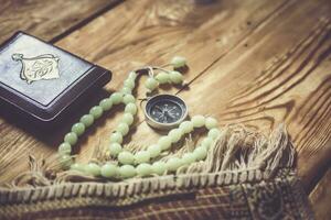 Traditional muslim prayer set bundle. Praying carpet, rosary beads, little version of the Holy Quran and qibla compass on wooden background. Free Space photo