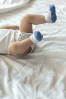 Legs of 6-8-month-old baby boy in white bodysuit playing in his bed. Copy space photo