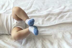 Legs of 6-8-month-old baby boy in white bodysuit playing in his bed. Copy space photo