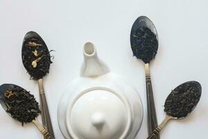 White ceramic tea pot and various dried teas on the white background. Flat lay view. Space for your text photo