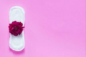 Sanitary napkin with red rose on it. On bright pink background. Period days concept showing feminine menstrual cycle. photo