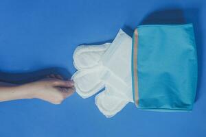 Young women taking sanitary pads inside of her cosmetic bag on blue background photo