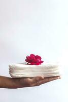 Woman's hand holding a stack of sanitary napkins with red rose on. Against white background. Period days concept showing feminine menstrual cycle. photo