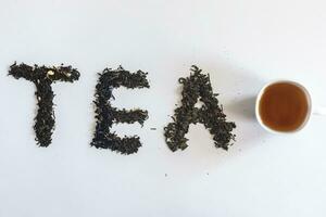 The word tea made with dry tea leafs and a cup of black tea photo