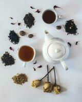 té conjunto con blanco cerámico té maceta, seco Rosa flores y otro té ingredientes en el blanco. plano laico ver de varios seco tés y tetera. ver desde arriba. espacio para tu texto foto