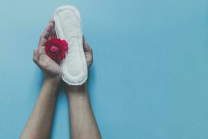 Female's hand holding sanitary napkins with red rose on it. Period days concept showing feminine menstrual cycle. Female's hygiene photo