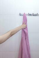 Young female after shower. Woman's wet hand taking her pink bathrobe hanging on a hook. Taking bathrobe after shower photo