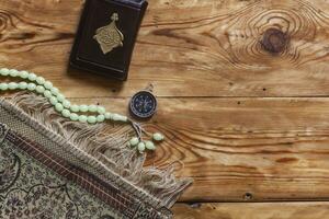 Traditional muslim prayer set bundle. Praying carpet, rosary beads, little version of the Holy Quran and qibla compass on wooden background. Free Space photo