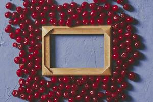 Wooden frame with copy space and ripe cherries on blue background. Berries and fruits around the empty wood frame photo