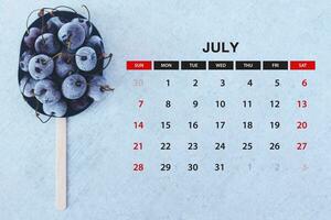 July calendar. Stack of frozen sweet cherries with July month calendar. Summer photo