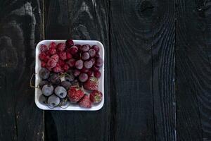 Homemade fresh frozen fruits. Healthy sweet dessert on dark rustic wood. photo