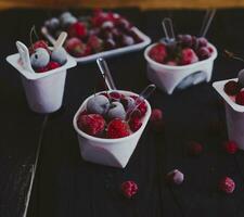 Homemade fresh yogurt. Healthy sweet dessert on dark rustic wood. Frozen fruits photo