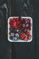 Homemade fresh frozen fruits. Healthy sweet dessert on dark rustic wood. photo