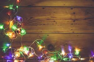 Christmas decorative lights. Christmas garland lights on wood. Colorful Xmas light bulbs on rustic brown plank photo