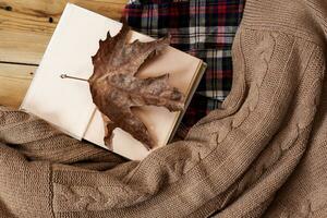 Fall background. Opened book and a big dry fall leaf. Knitted sweater photo