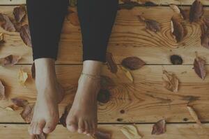 The feet of the person on the wooden floor covered with fall leaves. Autumn season concept with copy space photo