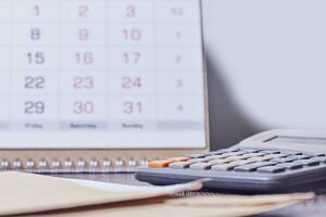 Calendar, calculator and stack of coins in office photo