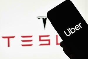 A person holds smartphone with Uber trademark with Tesla logo photo