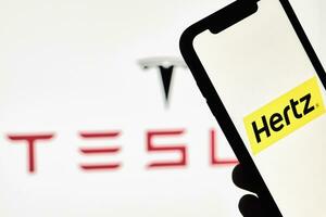 A person holds smartphone with Hertz trademark over big Tesla logo photo