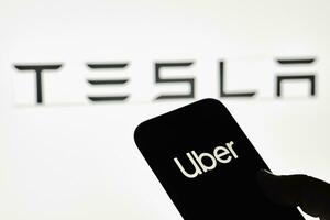 un persona sostiene teléfono inteligente con uber marca comercial con tesla logo foto