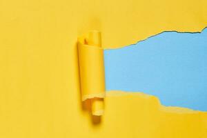 Torn piece of yellow paper over blue background photo