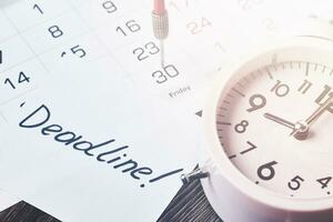 fecha límite texto en pedazo de papel, alarma reloj y mensual calendario foto
