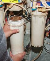 Women's hands remove flasks with contaminated water purification filters to be replaced with clean ones. The process of replacing the cartridges of a multi-stage water filter. photo