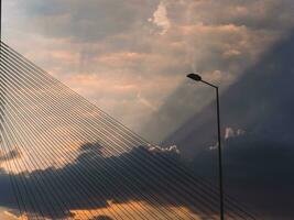 Lightpost and suspension bridge cables with sunbeams bursting through the clouds photo