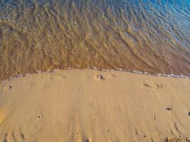 pequeño ola Lavado lejos huellas en el arena - en el playa foto