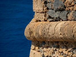 Decorative detail in the ancient fort wall in Crete, Greece - blue sea in the background photo