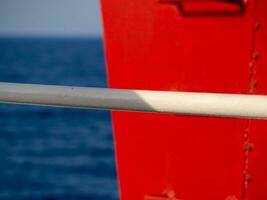 White handlebar railing in front of the red metal parts of the ship - sea in the background photo
