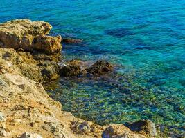 Amazing crystal clear blue water and sharp rock edges on the shore photo