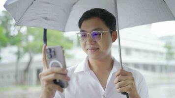 homme en portant parapluie dans pluvieux ville en marchant sur orateur avec La technologie mobile téléphone video
