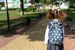 alumno con mochila y en un colegio uniforme en colegio yarda espalda a el marco. espalda a escuela, septiembre 1. un contento alumno. primario educación, elemental clase. la carretera a vida, a conocimiento foto