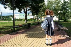 alumno con mochila y en un colegio uniforme en colegio yarda espalda a el marco. espalda a escuela, septiembre 1. un contento alumno. primario educación, elemental clase. la carretera a vida, a conocimiento foto