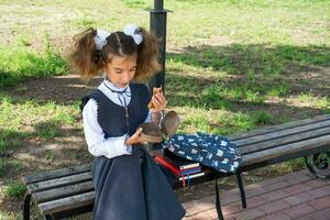 Girl with backpack eating sandwich packed in a sandwich box near school. A quick snack with a bun, unhealthy food, lunch from school. Back to school. Education, primary school classes, September 1 photo