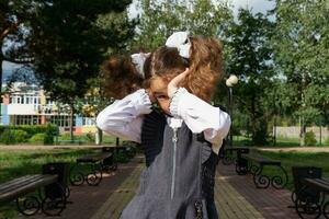 Girl with a backpack near the school after classes, unhappy, tired and headache. The child is crying, holding his head in his hands. Academic failures, poor grades, overwork photo